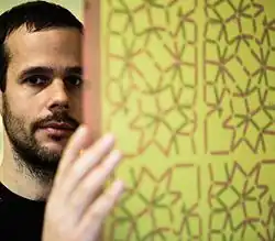 Federico Díaz standing beside a panel featuring intricate geometric patterns, partially obscuring his face.