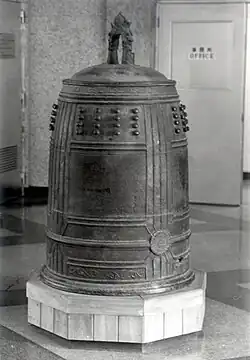 A black and white photo of a massive bronze bell on an indoor pedestal