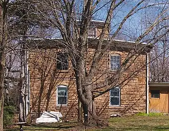 A two-story stone house with a cupola, partially obscured by a large tree