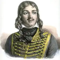 Color-tint print of a man with a moustache and hair reaching to his shoulders. He wears a dark hussar uniform of the 1790s.