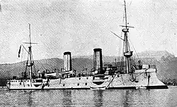 A light gray ship similar to the Forbin and Troude classes, with two funnels and two light masts sits at anchor.