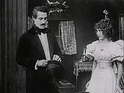 Black and white film still showing a man and woman in 1912 period costume