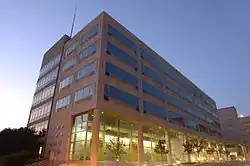 A six-story building of concrete and glass, as viewed from the front corner, with 14th Street parallel to the left face of the building. There are evenly spaced trees in front of the right face of the building.