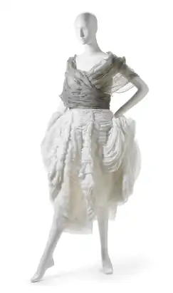 White mid-length sleeveless dress displayed on a mannequin. The skirt is made from numerous layers of thin fabric stacked to appear like a seashell.