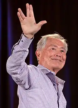 The image, taken at Phoenix Comicon, depicts actor George Takei waving at a crowd.