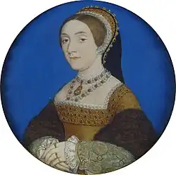 A portrait of a lady painted with her hands crossed at her waist and showing her from the waist up. She is wearing a gorgeous corseted dress, trimmed with pearls, with ornate cuffs trimmed with lace. She is wearing a pearl necklace and on her head is an ornate headband worn vertically, which is also trimmed with pearls.
