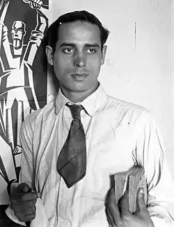 Photograph of Helios Gómez standing in front of one of his paintings