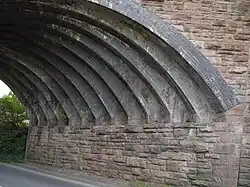 From a wall of stone, 13 narrow blue brick arch ribs spring. The spandrel wall, above, is also made of stone.