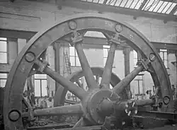 Flywheel; the hub and spokes cast in two halves, bolted at the hub with the rim assembled from ten castings. These are bolted to the spokes, held together by shrinking rings in the grooves.[80]