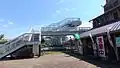 Station west entrance with the footbridge and entry to the level crossing. To the right is a shop for local products and also the kan'i itaku agent. The sign with the arrow says "JR tickets on sale (inside shop)".