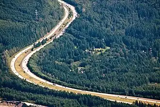 Aerial view of a freeway with two wide roadways set against trees