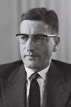Black-and-white portrait photograph of Nebenzahl, wearing a dark suit, white shirt, and patterned tie. He has short, combed hair and is wearing rectangular glasses. He is looking slightly to the side.
