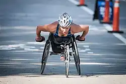 Women in blue and black clothes and a silver helmet racing in a black wheelchair.