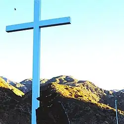 JPEGMafia pictured beside a similar white cross in a mountainous landscape at day. A small computer mouse is visible to the left of the cross