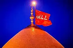 Red flag with "Ya Hussain" in white Arabic text flying from the dome of a mosque