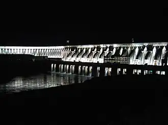 A gigantic concrete dam at night lit by powerful floodlights