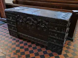 A large dark wooden chest carved with gothic tracery and animals sitting on a red and black tiled floor.
