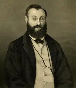 A sepia-toned, historical portrait of a bearded man wearing a suit and bow tie, with an indistinct facial expression.