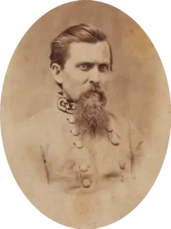 Sepia tone photo shows a frowning man with a beard and dark combed-back hair. He wears a gray uniform with three general's stars on the collar.