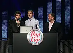 Three men stand behind a podium adorned with the PopCap Games logo.