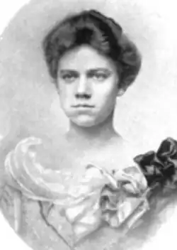 A young white woman with dark hair in an updo, wearing a light-colored dress with a dramatic wide neckline
