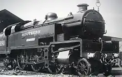 Side-and-front view of the 3-cylinder version of the locomotive. The distinguishing feature is a full-width flat panel rising vertically above the front buffer beam to the level of the bottom of the smokebox door. The water tanks are a different shape from the K Class, as they include a rectangular access hole in the side, bottom-front, for maintaining the valve gear, which is also different from the K class.