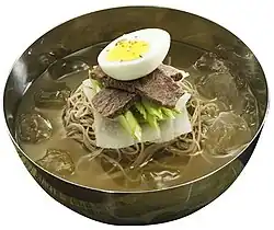 Naengmyeon (cold noodles) topped with boiled egg, pyeonyuk, cucumber, and pickled radish