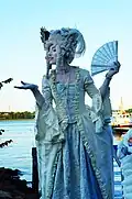 A woman performing as a living statue of Marie Antoinette is waving a hand fan