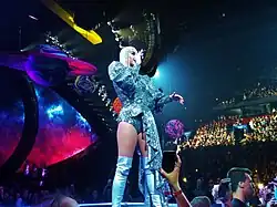 An image of Perry performing in front of an audience, wearing a metallic outfit with thigh-high boots.