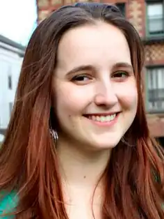 Headshot of Emily Temple-Wood standing outside. She is a young white woman with red hair wearing a green dress.