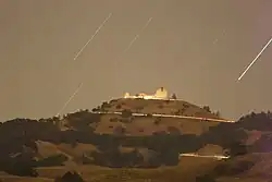 Time-lapse photograph of white buildings on top of a mountain at night with stars streaking across the sky.