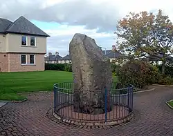 Tall stone standing upright with a metal fence around its perimeter.