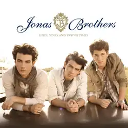 The three band members leaning forward on a flat surface, with a white background. The band's logo and album's name is display in the upper center.