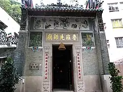 The exterior of a temple, with a large door flanked by Chinese characters. Other urban buildings can be seen in the background.