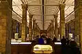 The first floor gallery in the east wing at the front of The Natural History Museum, with a typical Waterhouse white ceiling with geometrical patterning contrasting with the terracotta walls and columns, each column has a core of iron, supporting concrete vaults hidden by the ceiling, part of the fireproofing of the building