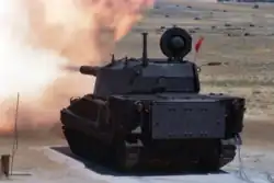 A black or dark-colored AGS fires its main gun at a range. The commander's hatch is open and there is no commander's armament present.