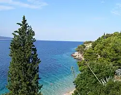 A photograph of a coastline with a light blue sky with white clouds above, a dark blue ocean on the left, and a sandy beach on the right
