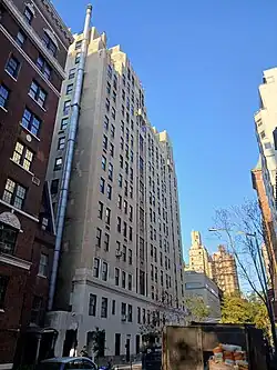 The Carlyle's apartment wing as seen from 77th Street, looking toward the west. The facade is made of beige brick with rectangular windows. A red-brick apartment building is visible at left, to the east of the hotel.