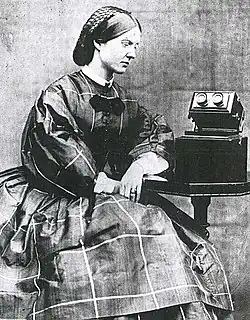 photograph of Mary Ward, seated and looking at a microscope on a table towards her left