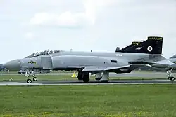 Side view of a Phantom FGR.2. The aircraft is in air superiority grey with a black tail, and has a tiger's head painted on the nose, and a tiger's head in a white disc on the tail. The radar warning receiver cap mounted on the top of the tail is painted with yellow and black tiger stripes. These markings represent Seventy-four Squadron