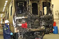 The burnt front of a train with a man wearing a helmet and mask looking at it from the left