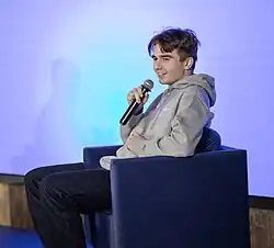 Side view of a smiling Michał Matczak, as he is participating in a panel during a conference