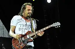 Michael Franti wearing a white t-shirt with handwritten slogans, playing an electric guitar onstage