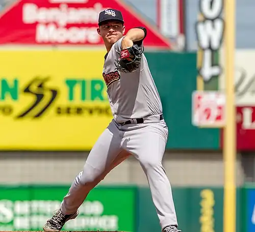 A baseball player in a white uniform, mid-pitch.