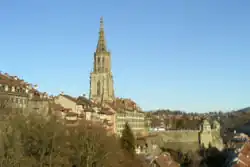 A grey stone Gothic spire rises above the Old City of Bern