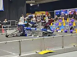 Three robots sit on the Charging Station, with one tipped over