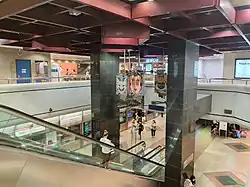 Photograph of the NSL platforms, decorated with diamond tiles, taken from the concourse. An escalator connects the concourse to the platforms. Between the two black pillars supporting the station's interior, the sculpture Lantern of Music by Tan Ping Chiang is suspended from the ceiling