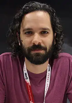 A 36-year-old man with curly black hair smirking at the camera.