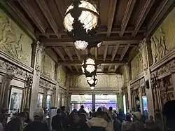 The theater's original lobby, facing north, with a crowd exiting toward 42nd Street at the end of a show. There are ticket booths and elevators to the right; the ticket booths are in the background, while the elevators are in the foreground.