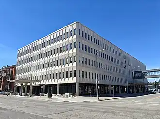 The front of a five-story concrete office building surrounded by construction fencing and equipment.